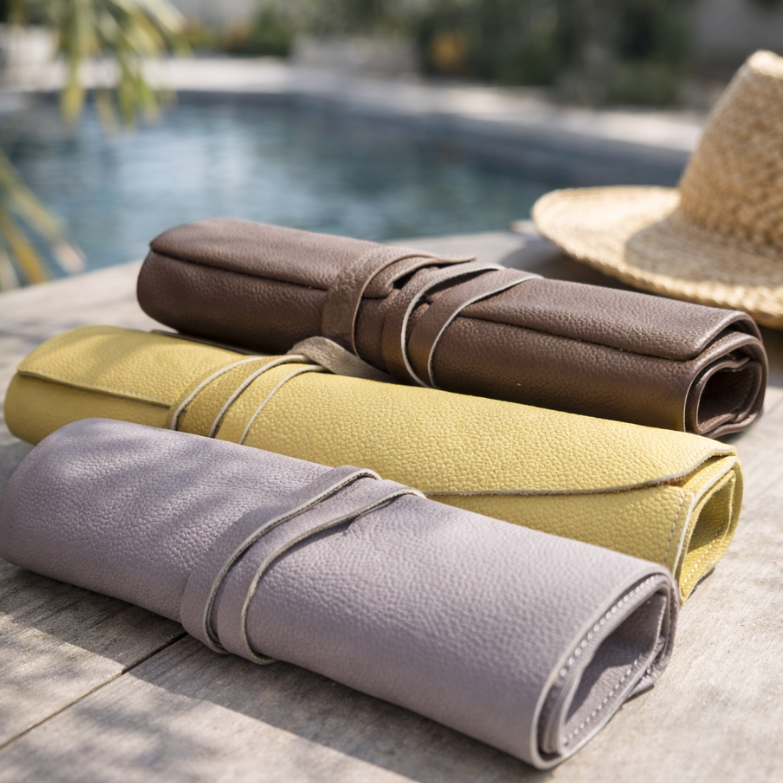 Three rolled-up leather mats in brown, yellow, and gray on a wooden surface near a pool.